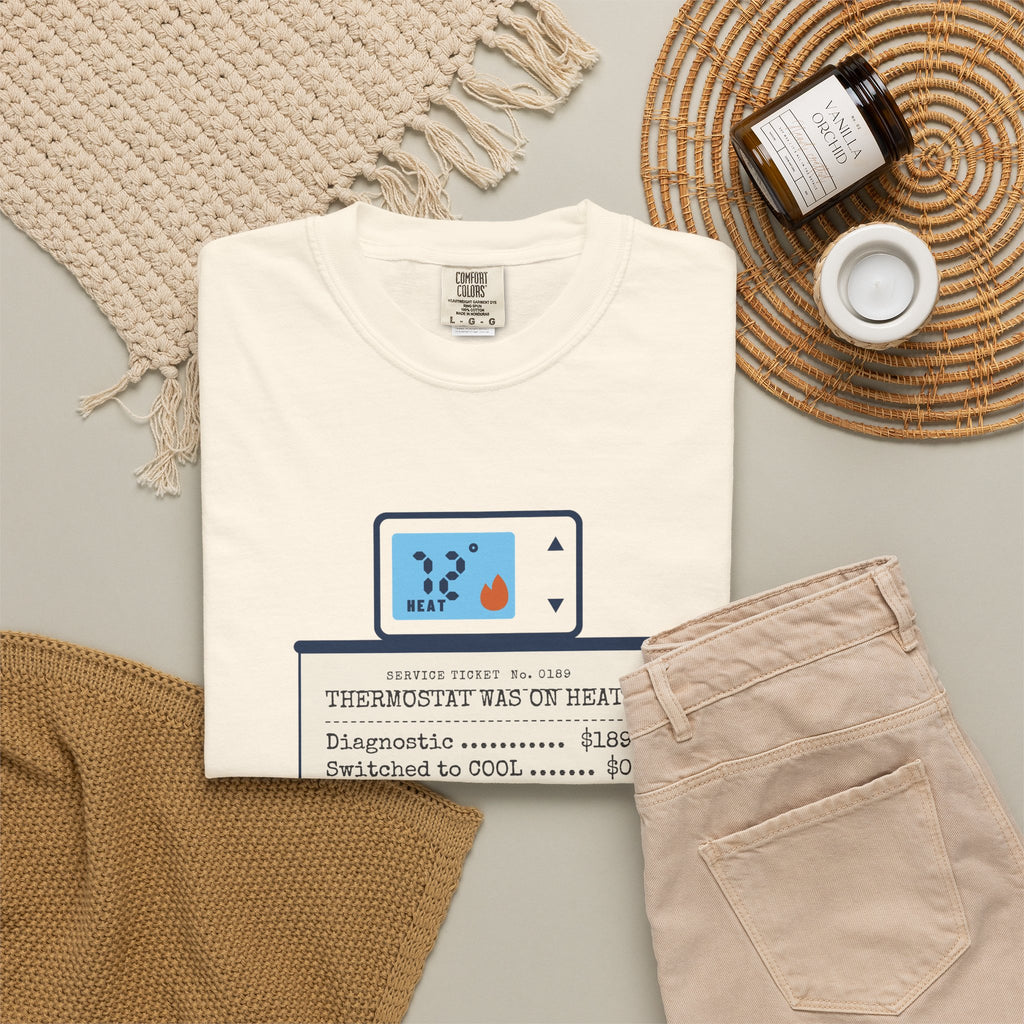 Folded ivory t-shirt reading Thermostat Was on Heat. Diagnosis: $189. with a simple thermostat graphic