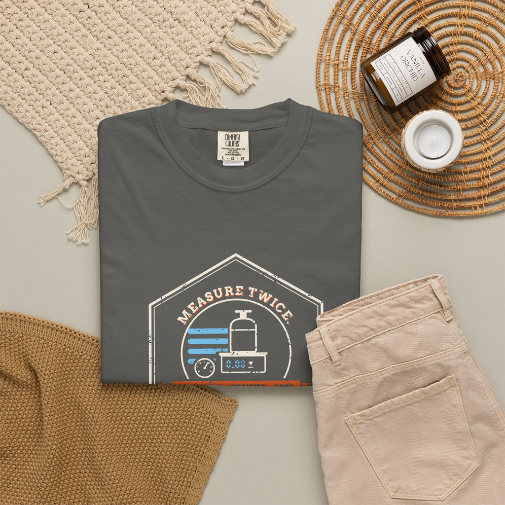 Faded black t-shirt flat-lay with a retro Measure Twice. Charge Once. hex badge with a cylinder on a scale
